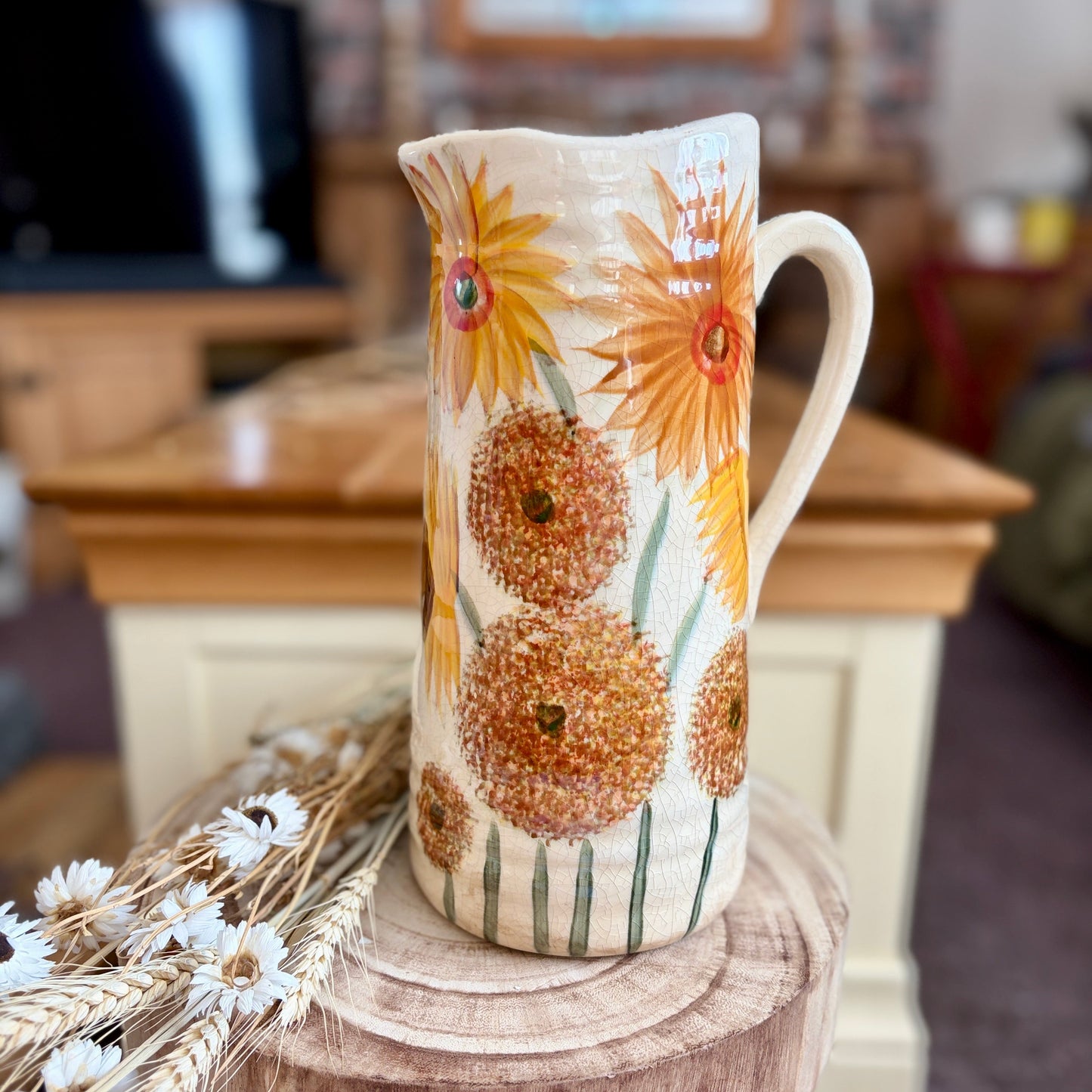 Decorative ceramic pitcher with floral design on a wooden stool in a home setting.