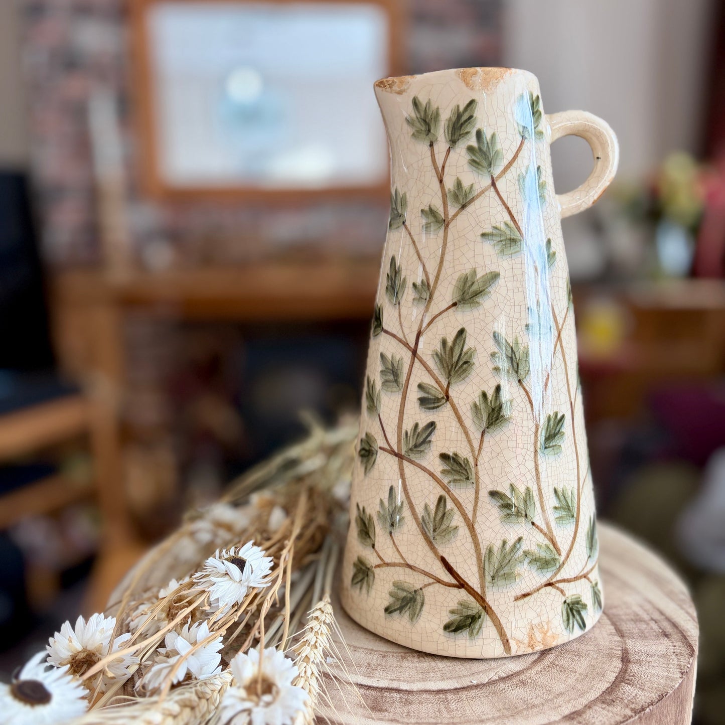Ceramic vase with leaf pattern on a wooden stool in a home setting
