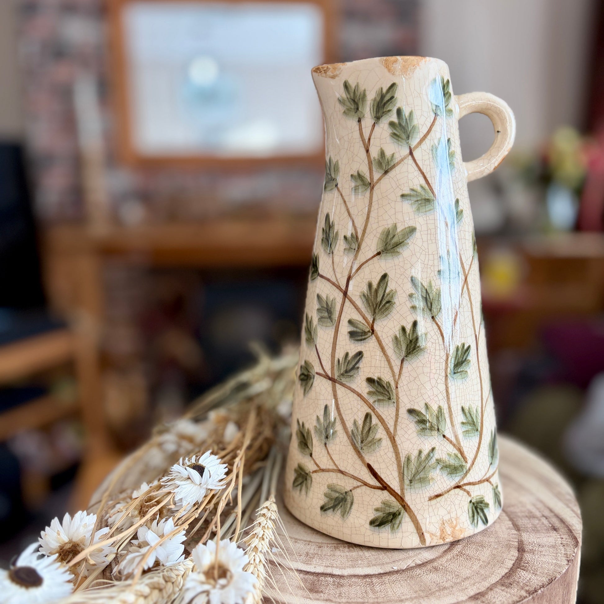 Ceramic vase with leaf pattern on a wooden stool in a home setting