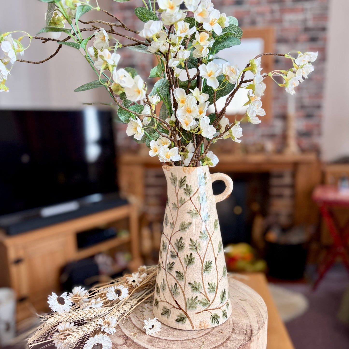 Decorative vase with green leaf design on a wooden stool in a living room setting.