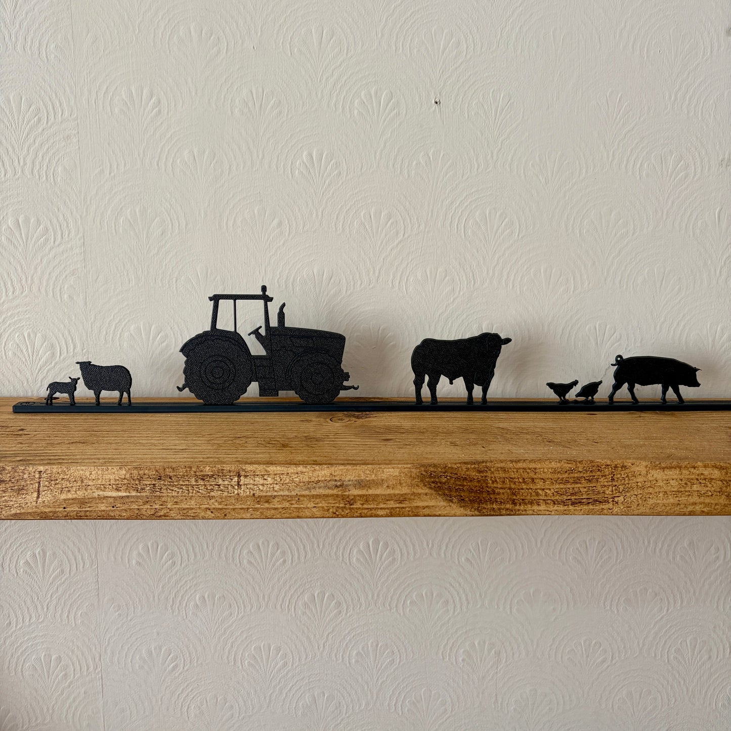 Silhouette models of a tractor and farm animals on a wooden shelf against a white wall.