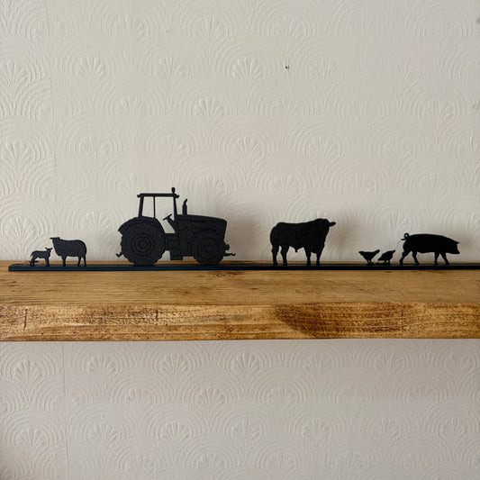 Silhouette models of a tractor and farm animals on a wooden shelf against a white wall.