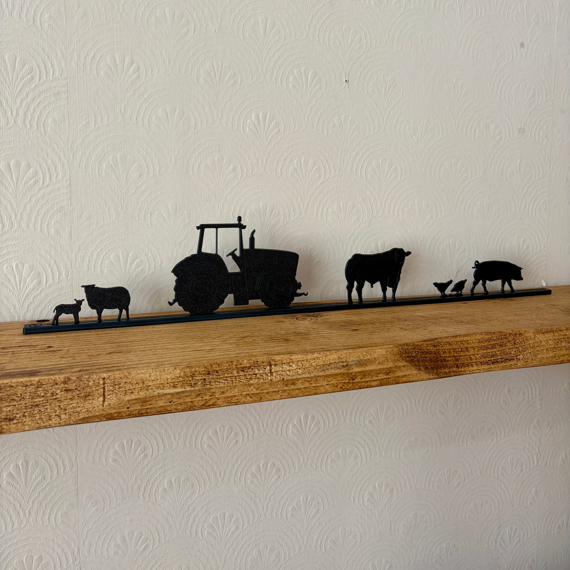 Silhouette decorations of a tractor and farm animals on a wooden shelf against a white wall.