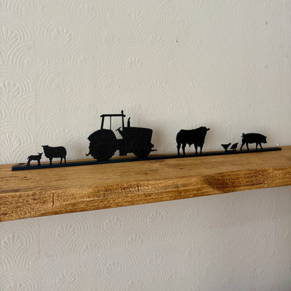 Silhouette decorations of a tractor and farm animals on a wooden shelf against a white wall.