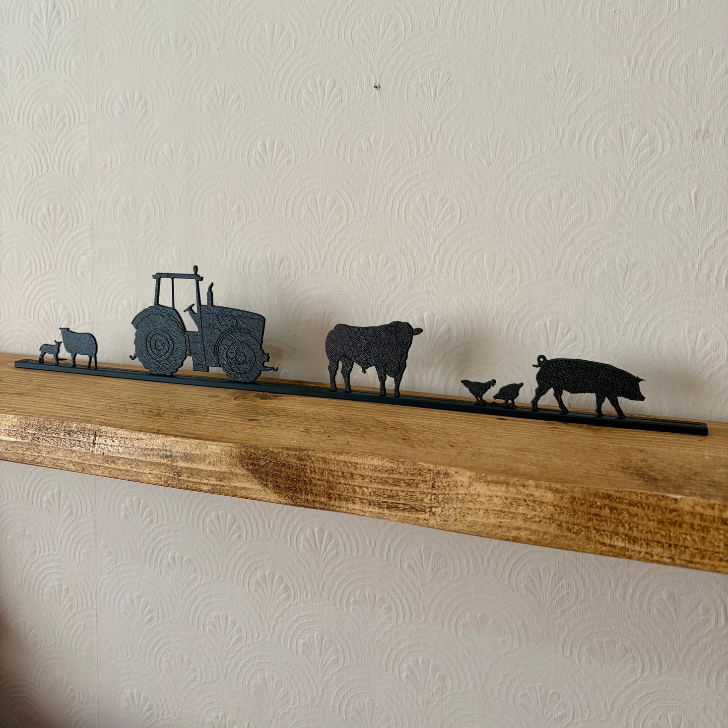 Decorative recycled plastic farm animal silhouettes on a wooden shelf against a white wall.