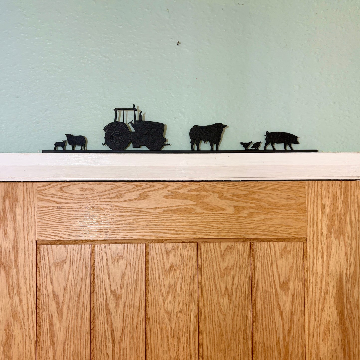Wooden door with decorative black recycled plastic silhouettes of a tractor, cows, and calves on a white surface.