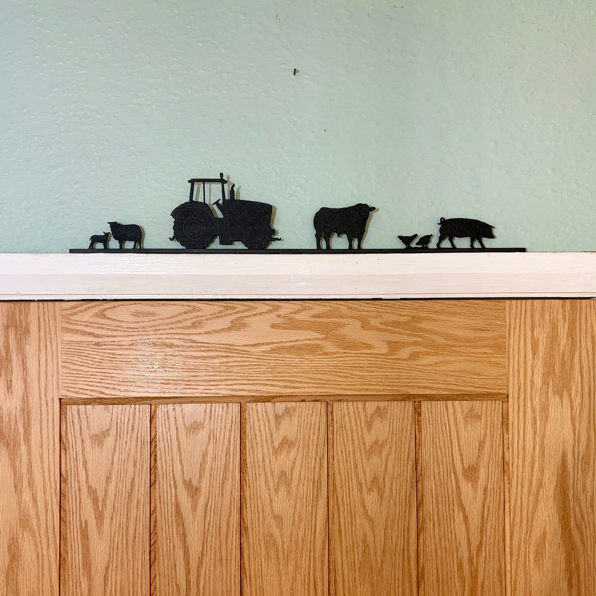 Wooden door with decorative black recycled plastic silhouettes of a tractor, cows, and calves on a white surface.