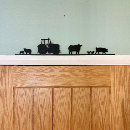 Wooden door with decorative black recycled plastic silhouettes of a tractor, cows, and calves on a white surface.