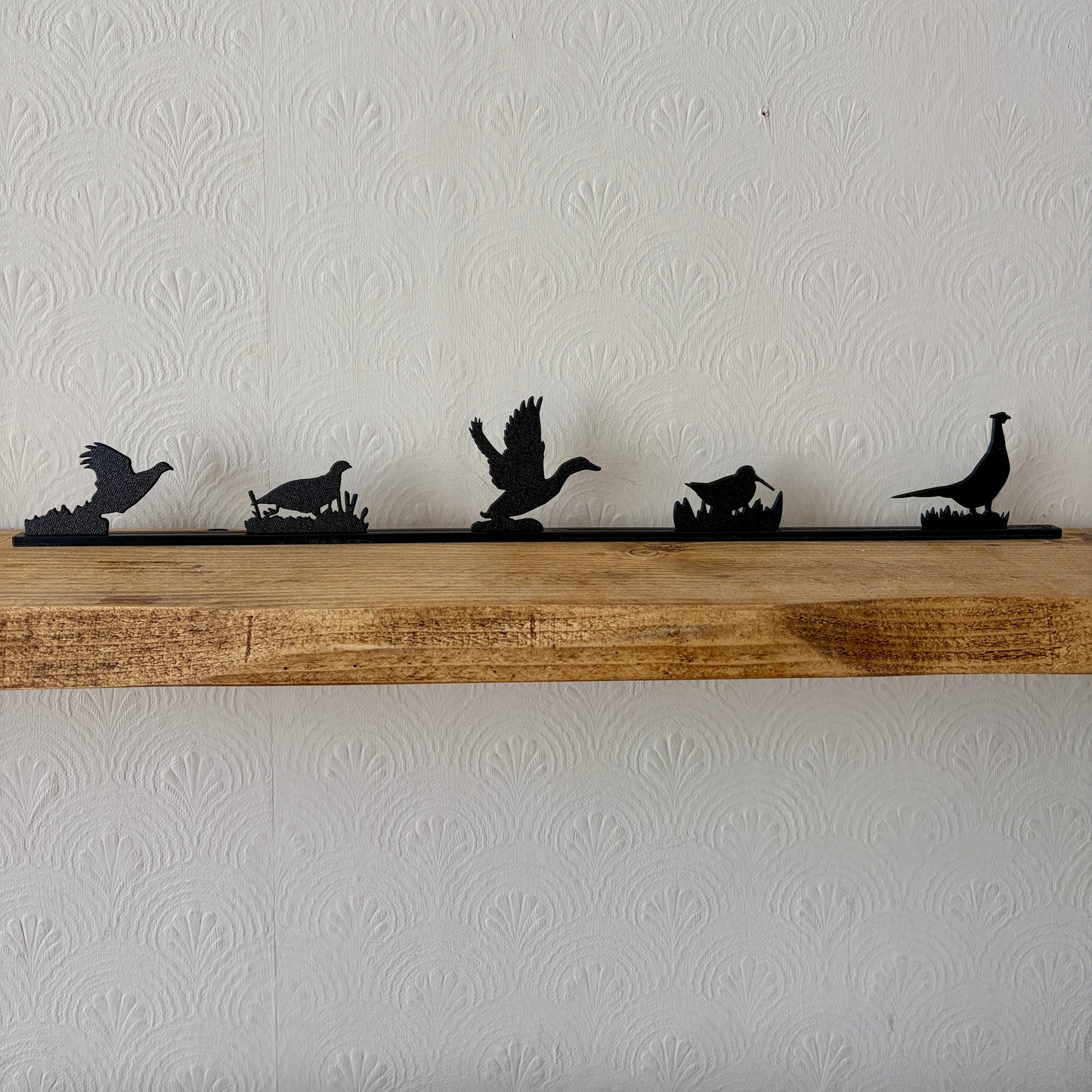A set of five black game bird silhouettes mounted on a rustic wooden shelf against a white textured wall.