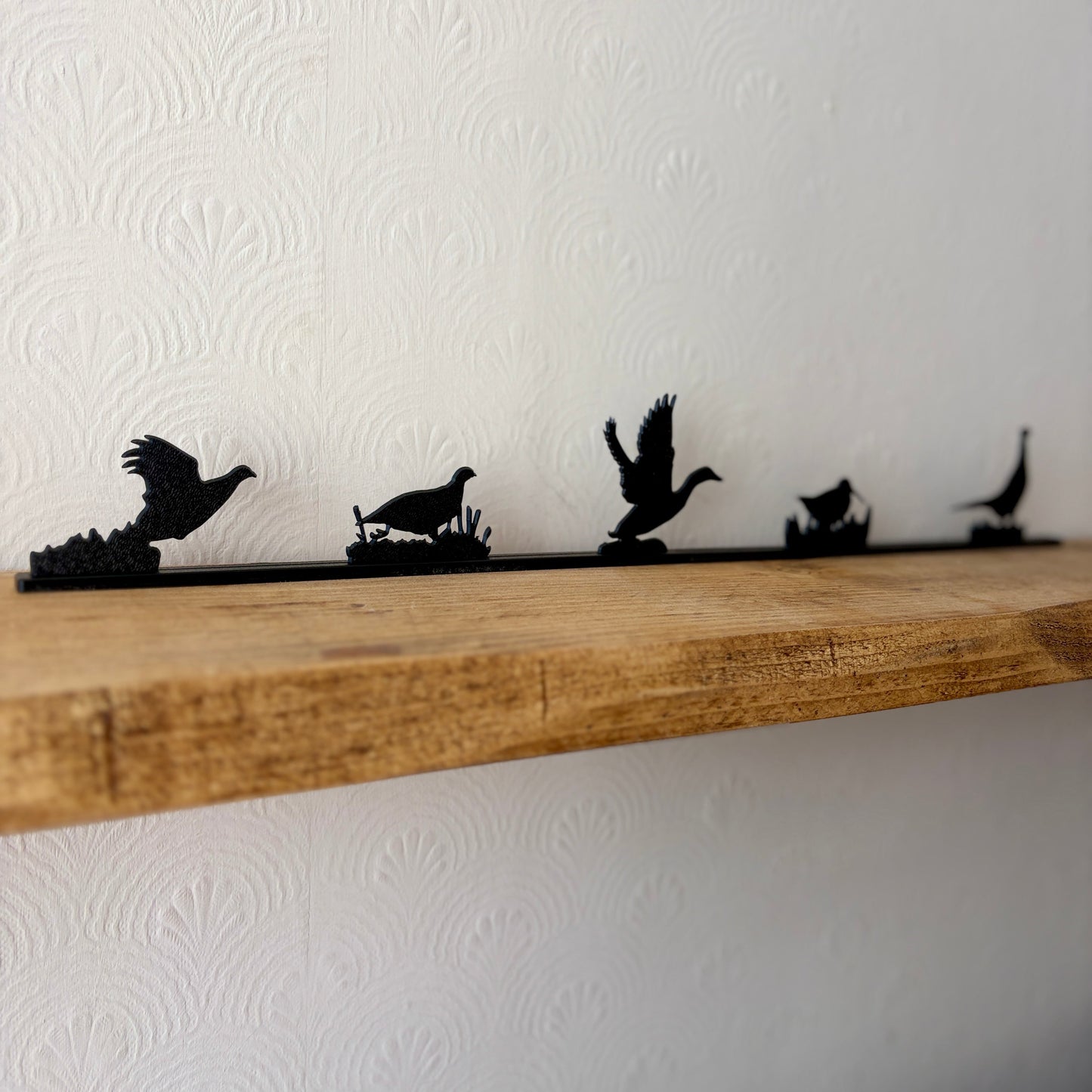 Black wall shelf decor featuring silhouettes of five game birds in flight and standing poses, mounted on a rustic wooden shelf against a white textured wallpaper background.