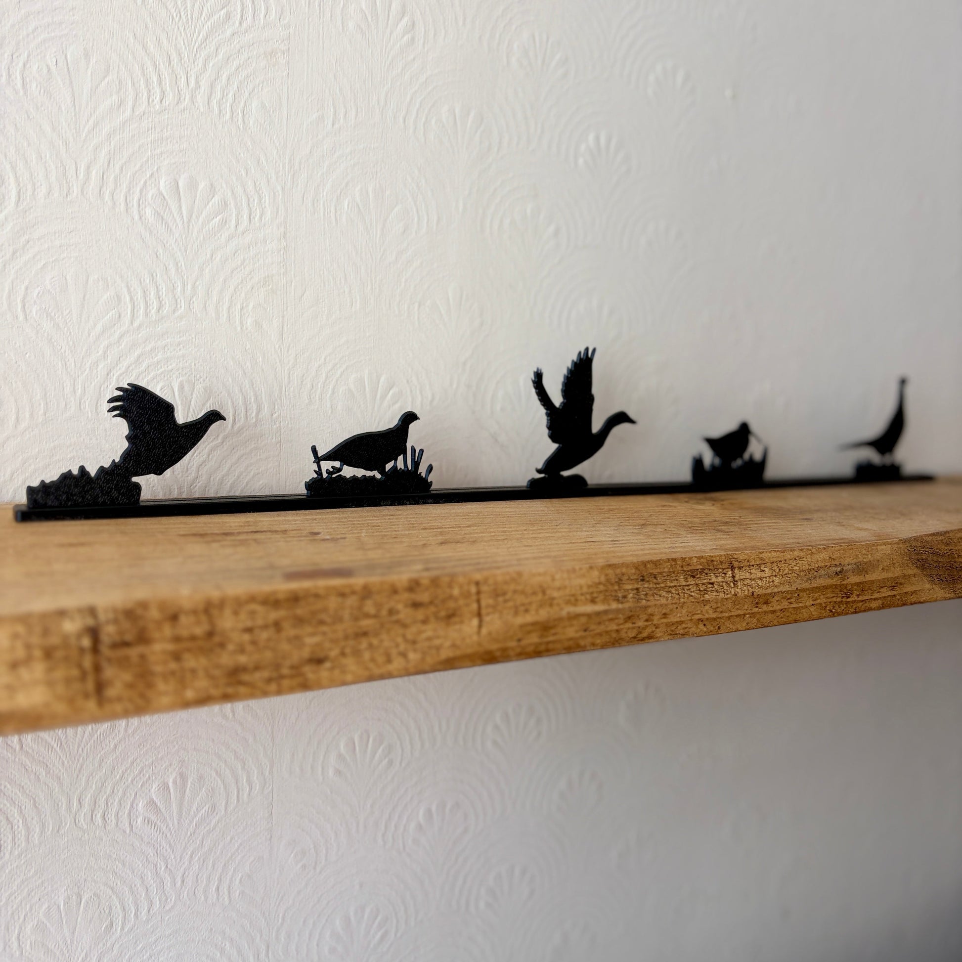 Black wall shelf decor featuring silhouettes of five game birds in flight and standing poses, mounted on a rustic wooden shelf against a white textured wallpaper background.