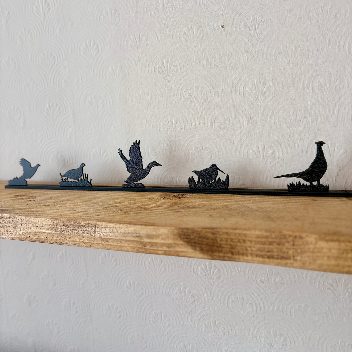 A black wall shelf topper featuring silhouettes of various game birds, displayed on a rustic wooden shelf against a white textured wall.