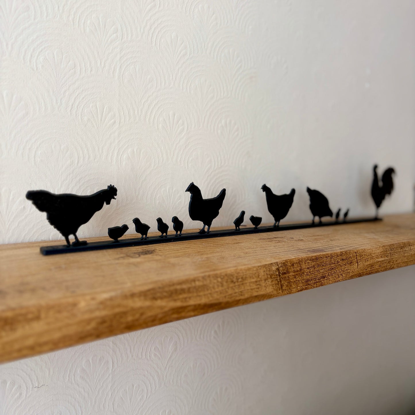 Black recycled plastic topper of a family of chickens and chicks, displayed on a rustic wooden shelf against a white textured wall.