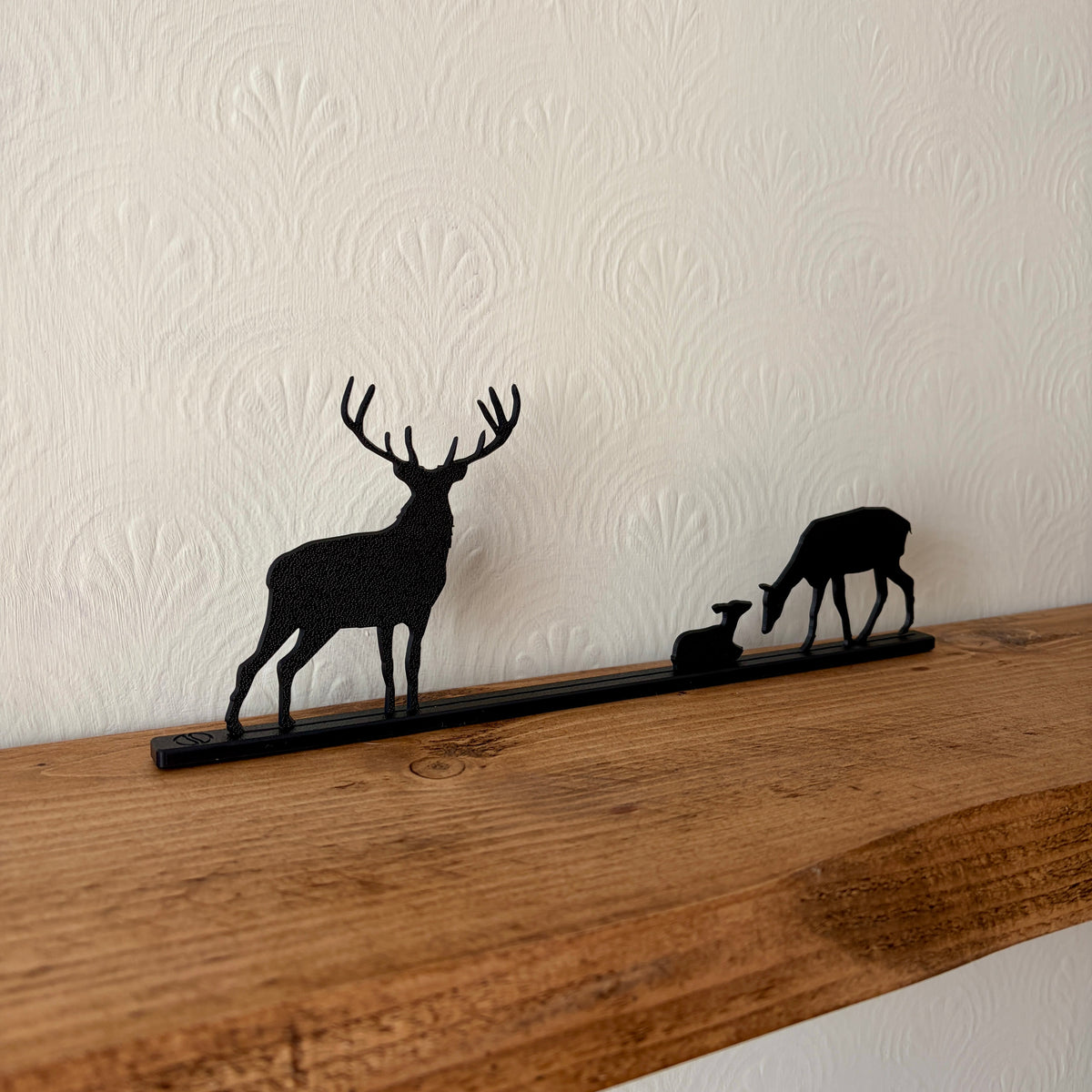 A black recycled plastic deer silhouette shelf mounted on a rustic wooden mantel against a white textured wallpaper background.