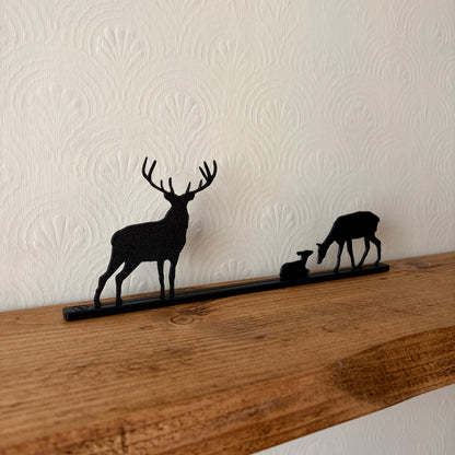 A black recycled plastic deer silhouette shelf mounted on a rustic wooden mantel against a white textured wallpaper background.
