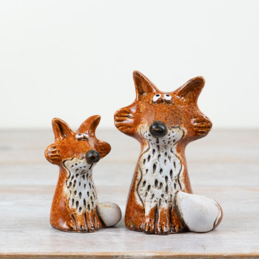 Two ceramic fox figurines on a wooden surface with a light background