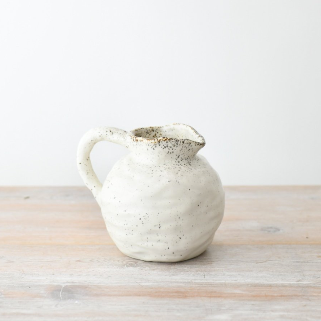 Round speckled ceramic jug on a wooden surface with a white background