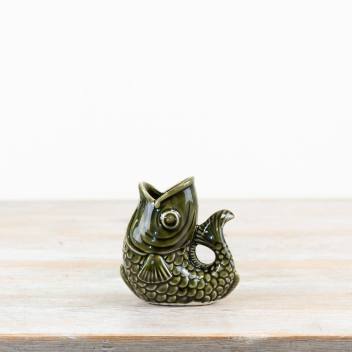 Ceramic fish jug in forest green on wooden surface, perfect for pouring or displaying flowers.