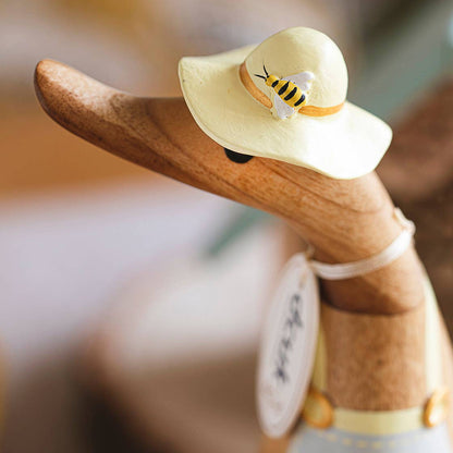 Wooden duck figurine wearing a yellow hat with a bee design on a blurred background