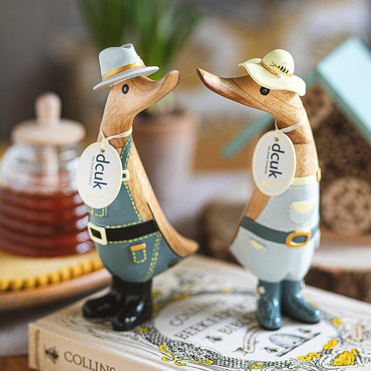 Two wooden duck figurines wearing hats on a book with flowers in the background