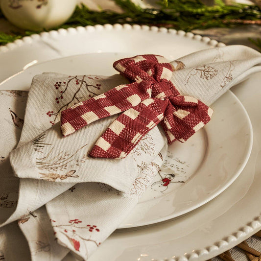 A close-up of a styled table setting featuring a folded cream linen napkin with a red and cream gingham bow, resting on a white plate.